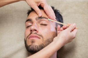 Hombre con esteticista depilando sus cejas con cera